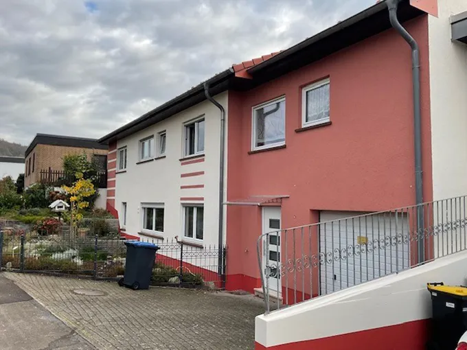 Zweistöckiges Wohnhaus mit rotem Dach, heller, zweifarbiger Fassade und mehreren Fenstern, Seitenansicht